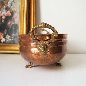 May include: A copper planter with brass handles and feet. The handles are shaped like lion heads. The planter has a hammered finish.