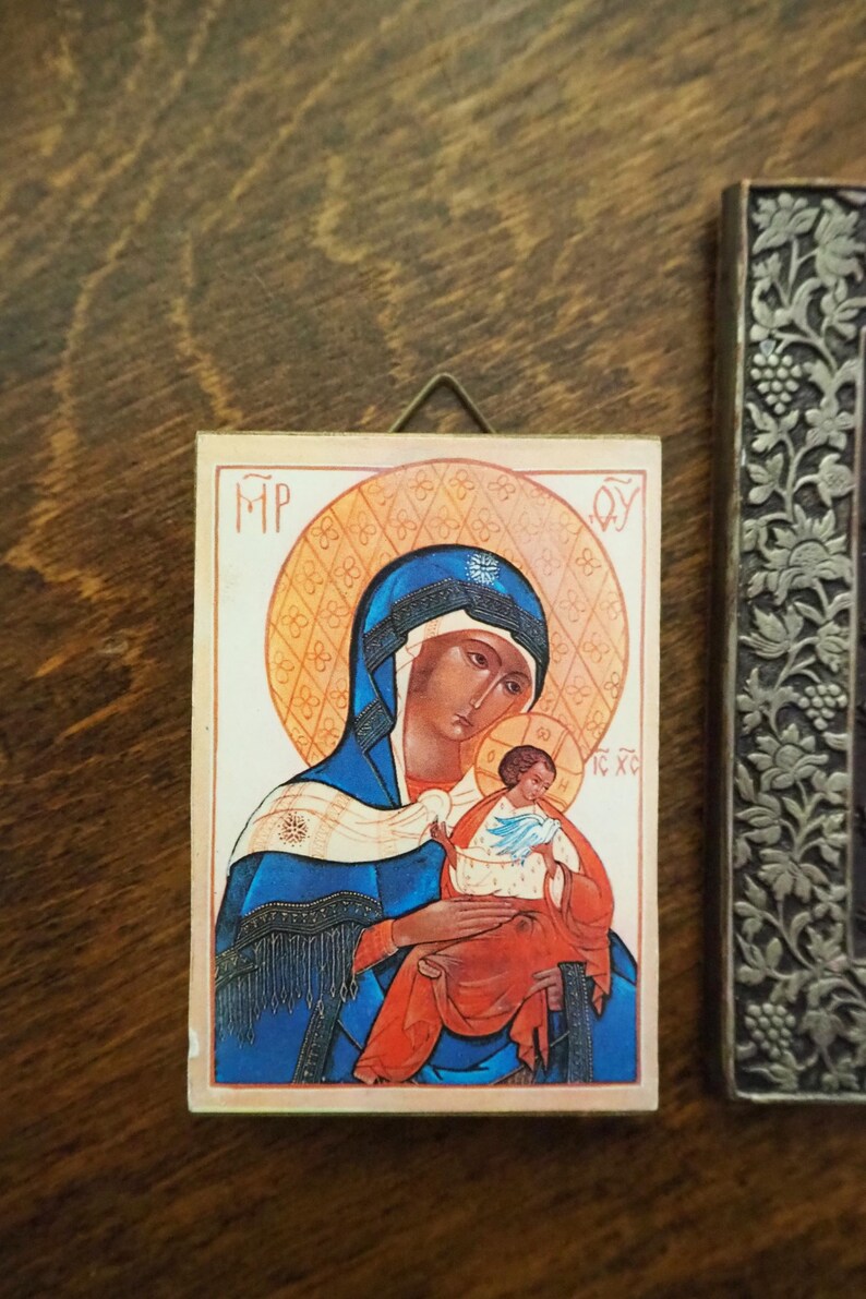 Pu&ograve; includere: Un'icona religiosa che raffigura la Vergine Maria che tiene in braccio il bambino Ges&ugrave;. L'icona &egrave; dipinta in uno stile tradizionale con accenti dorati e uno sfondo bianco. Il testo "MP OY IC XC" &egrave; visibile sull'icona.