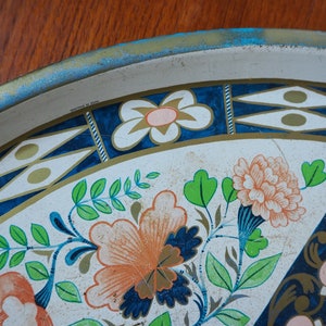 Puede incluir: Una bandeja de servir de metal blanco con un dise&ntilde;o floral azul y dorado. La bandeja tiene un borde azul y dorado con fondo blanco. El dise&ntilde;o floral presenta flores rosas, naranjas y verdes.