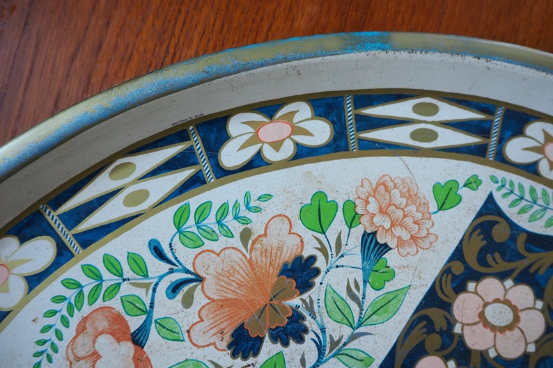 Puede incluir: Una bandeja de servir de metal blanco con un dise&ntilde;o floral azul y dorado. La bandeja tiene un borde azul y dorado con fondo blanco. El dise&ntilde;o floral presenta flores rosas, naranjas y verdes.