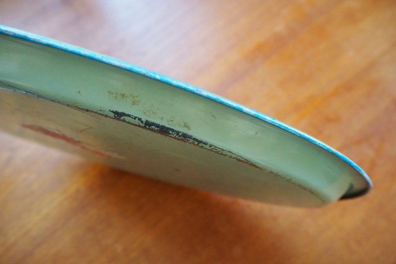 Puede incluir: Una bandeja de metal verde claro con un borde turquesa. La bandeja tiene una superficie ligeramente desgastada.