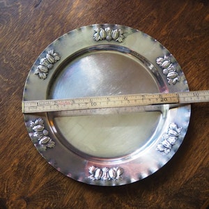May include: A silver serving tray with a decorative border of embossed leaves and berries. The tray is 8 inches in diameter.