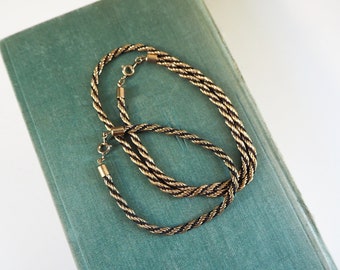 May include: Two gold rope chains with black accents, lying on a green surface.