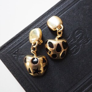 May include: A pair of gold-tone earrings with black enamel hearts. The hearts have a geometric pattern of black dots and a star.