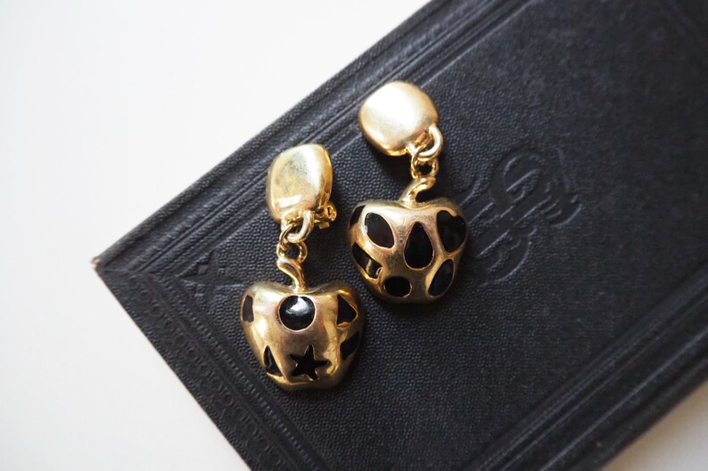 May include: A pair of gold-tone earrings with black enamel hearts. The hearts have a geometric pattern of black dots and a star.