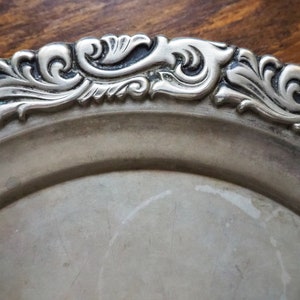 May include: A silver serving tray with a decorative, ornate rim. The rim is detailed with a swirling, floral design.