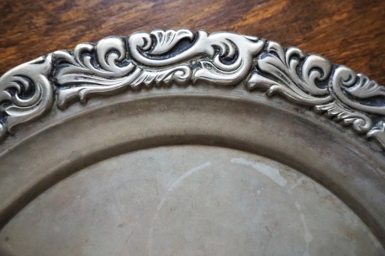 May include: A silver serving tray with a decorative, ornate rim. The rim is detailed with a swirling, floral design.