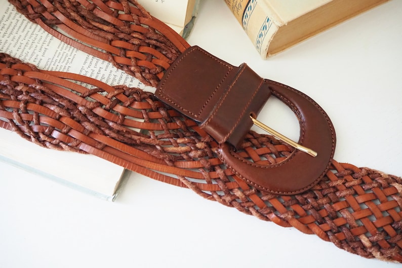 May include: A brown leather belt with a woven design and a large, brown leather buckle with a gold metal clasp.