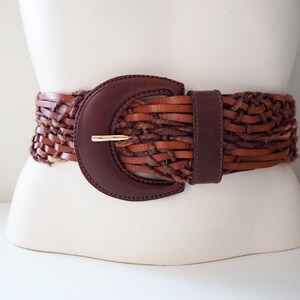 May include: A brown leather braided belt with a large, dark brown, rounded buckle.