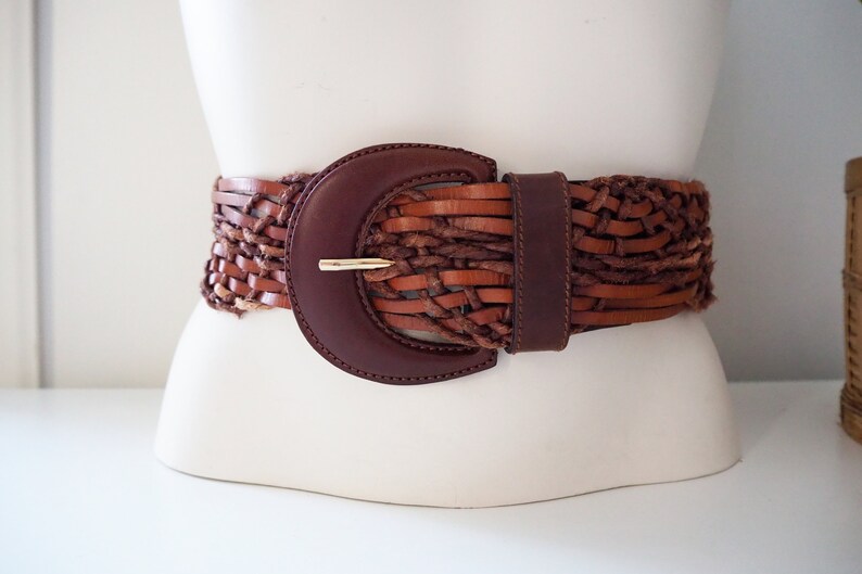 May include: A brown leather braided belt with a large, dark brown, rounded buckle.