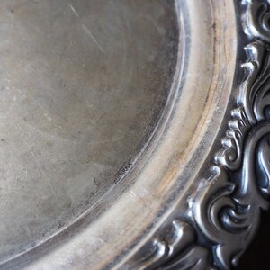 May include: A silver serving tray with a decorative, ornate border. The tray has a smooth, polished surface.