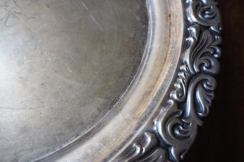 May include: A silver serving tray with a decorative, ornate border. The tray has a smooth, polished surface.