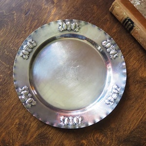 May include: A silver serving tray with a scalloped edge and a decorative design of clusters of berries around the rim.
