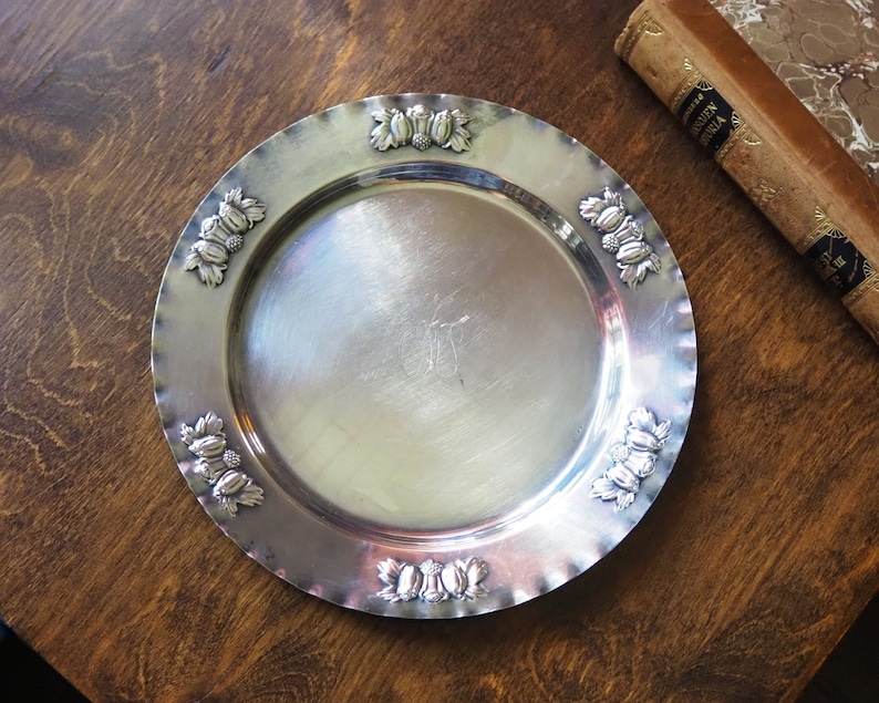 May include: A silver serving tray with a scalloped edge and a decorative design of clusters of berries around the rim.