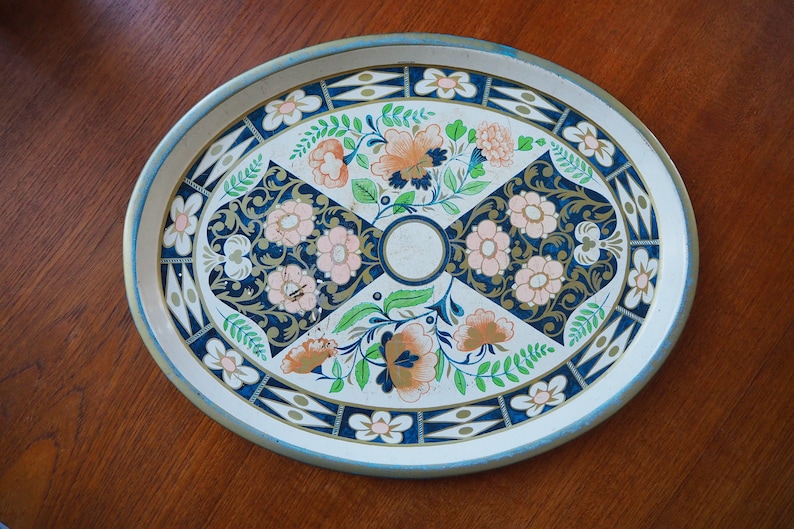 Puede incluir: Una bandeja de servir ovalada de metal con fondo blanco y un dise&ntilde;o floral en tonos azules, verdes, rosas y naranjas. El dise&ntilde;o presenta flores, hojas y espirales estilizadas.