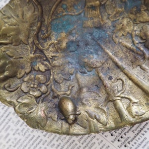 May include: A vintage brass trinket dish with an ornate design featuring leaves, flowers, and a small snail. The dish has a worn, aged patina.