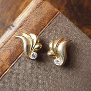 May include: A pair of gold-tone earrings with a leaf design and a clear rhinestone in the center of each earring.