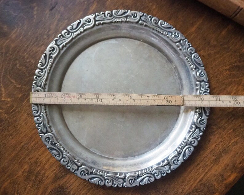 May include: A silver serving tray with an ornate, embossed design around the edge. The tray measures approximately 8 inches in diameter.