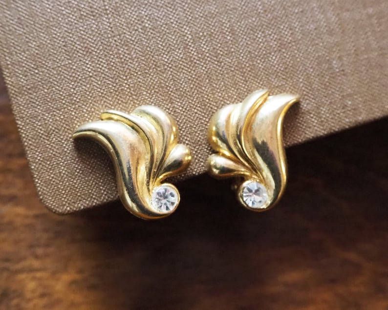 May include: A pair of gold-tone earrings with a leaf design and a clear rhinestone in the center of each earring.