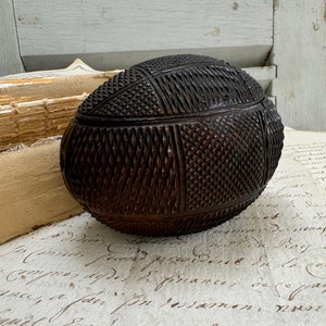 May include: A dark brown, intricately carved wooden egg-shaped box. The box has a geometric pattern carved into its surface.