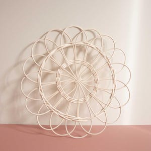 May include: White wicker wall decor in the shape of a flower with a circular center.