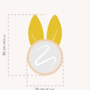 May include: A whimsical illustration of a bunny face with yellow ears and a white face with a wavy design. The bunny is 10.2 inches tall and 6.3 inches wide.