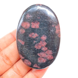 Peut inclure: Une pierre lisse de forme ovale avec une base gris foncé et des taches roses et rouges éparses.