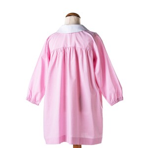 Puede incluir: Vestido de cuadros vichy rosa y blanco con cuello blanco. El vestido tiene mangas largas y una falda fruncida.