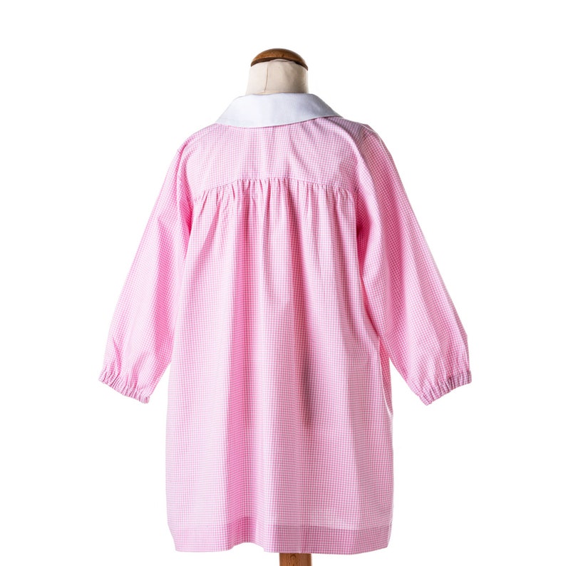 Puede incluir: Vestido de cuadros vichy rosa y blanco con cuello blanco. El vestido tiene mangas largas y una falda fruncida.