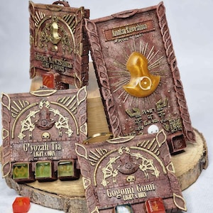 May include: Four intricately designed, rectangular, brown and gold decorative boxes with text and symbols. Each box has a different design and text, including "Amatsu Kuwashima", "C'yozah Tia", and "Gogomi Gomi". Some boxes have small, colorful cubes.