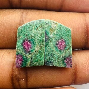 Puede incluir: Dos cabujones de piedra preciosa verde y rosa con un patrón único. Los cabujones están cortados en forma rectangular con bordes redondeados.
