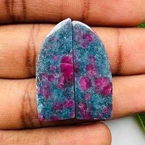May include: Two cabochon gemstone halves, one blue-green with pink flecks and the other pink with blue-green flecks.