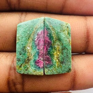 May include: Two green and pink gemstone cabochons with a rectangular shape. The cabochons are cut in half and show a pink and green pattern.