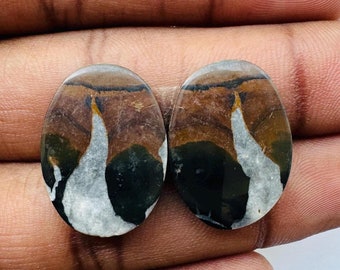 May include: Two oval-shaped, polished, natural stone cabochons with a unique, abstract pattern in shades of brown, black, and white. The stones have a smooth, glossy finish.