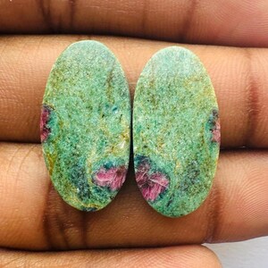 Può includere: Due pietre preziose verdi di forma ovale con inclusioni rosa e bianche. Le pietre sono tagliate a cabochon.