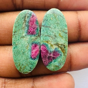 Peut inclure: Deux pierres précieuses vertes de forme ovale avec des inclusions roses et rouges. Les pierres sont serties dans un sertissage argenté.