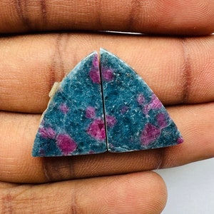 Puede incluir: Dos piezas triangulares de piedra preciosa verde y rosa, probablemente rubí, con un acabado rugoso y natural.