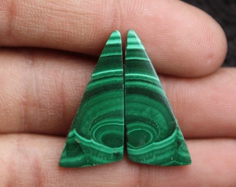 May include: Two triangular malachite gemstones with a vibrant green color and intricate banded patterns. The polished stones are displayed against a neutral background, showcasing their natural beauty and unique mineral formations.