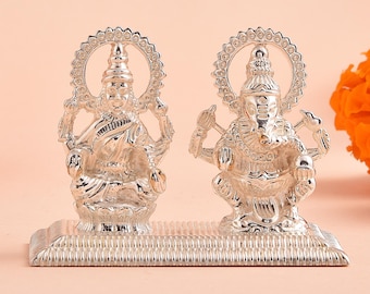 Può includere: Statua argentata di Lakshmi e Ganesha, divinità indù, sedute su una base argentata. Le statue sono dettagliate e ornate, con disegni intricati e una finitura lucida.