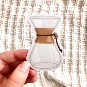 May include: A clear glass pour-over coffee maker with a brown band and a brown string tied around the top.