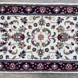 May include: A white runner rug with a floral pattern in shades of red, brown, and blue. The rug has a fringe border and is approximately 2 feet by 4 feet.