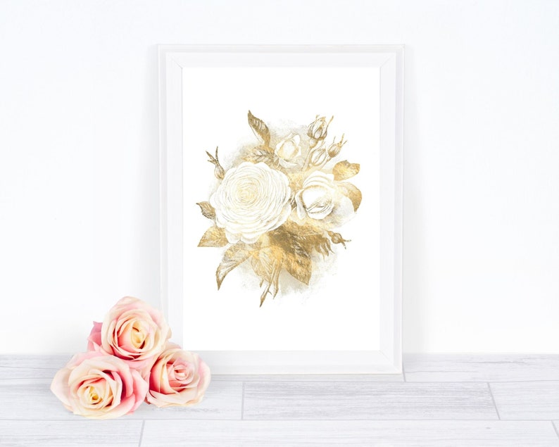 May include: A framed floral art print featuring a watercolor illustration of white roses and gold leaves. The artwork is displayed in a white frame. Three pink roses are in the foreground, adding a touch of color to the composition.