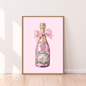 May include: A pink champagne bottle with a gold label and a pink ribbon bow. The bottle is illustrated with pink flowers and green leaves.