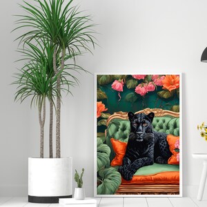 Pode incluir: Uma pantera negra est&aacute; sentada em um div&atilde; de veludo verde com almofadas laranja. O div&atilde; &eacute; cercado por folhagem verde exuberante e flores cor-de-rosa.