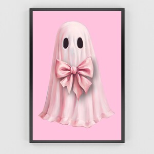 Op de afbeelding: Een ingelijste kunstdruk met een grillige spookillustratie. Het spook is afgebeeld in een zachtroze laken met een grote roze strik. De achtergrond is effen roze en het kunstwerk is ingelijst in een zwarte lijst.