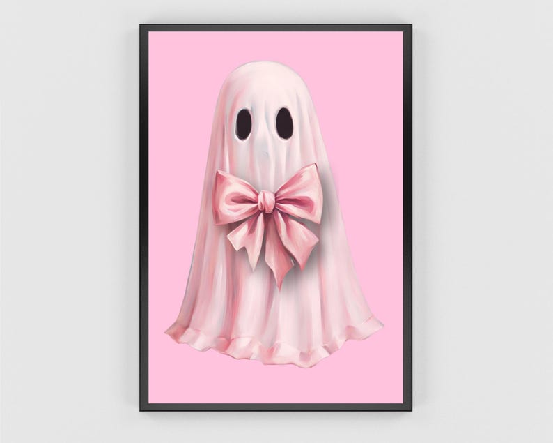 Op de afbeelding: Een ingelijste kunstdruk met een grillige spookillustratie. Het spook is afgebeeld in een zachtroze laken met een grote roze strik. De achtergrond is effen roze en het kunstwerk is ingelijst in een zwarte lijst.