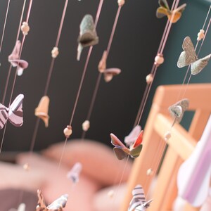 Puede incluir: Un m&oacute;vil con mariposas de papel de colores que cuelgan de cuerdas con cuentas de madera. Las mariposas son de varios patrones y colores, incluyendo naranja, verde, negro y blanco.