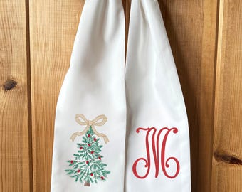 May include: White Christmas-themed table runner with a green embroidered Christmas tree design, red berries, and a tan bow. The right side features a red monogram letter "M".