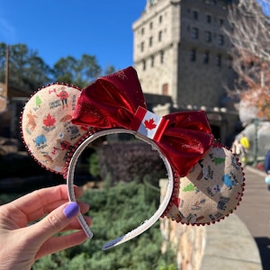 May include: Red and white Minnie Mouse ears with a Canadian flag bow and a beige ear featuring a map of Canada with various Canadian icons.