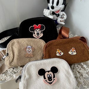 May include: Four different plush crossbody bags with various Disney character patches. The bags are beige, brown, black, and white. The patches include Mickey Mouse, Minnie Mouse, a bear, and Chip and Dale.
